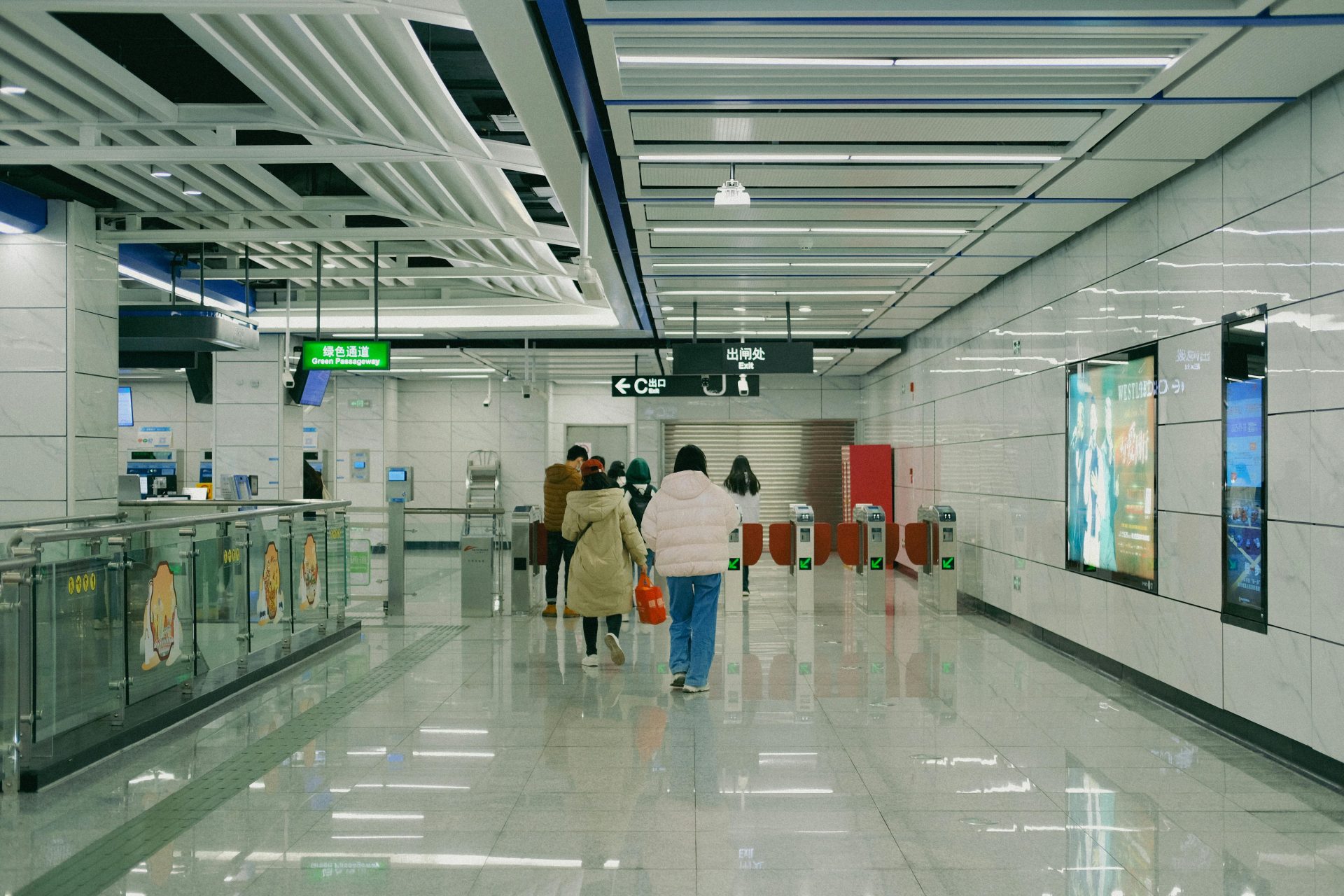 Des passagers traversent le couloir moderne d'une station de métro équipée de panneaux d'affichage électroniques et de tourniquets.